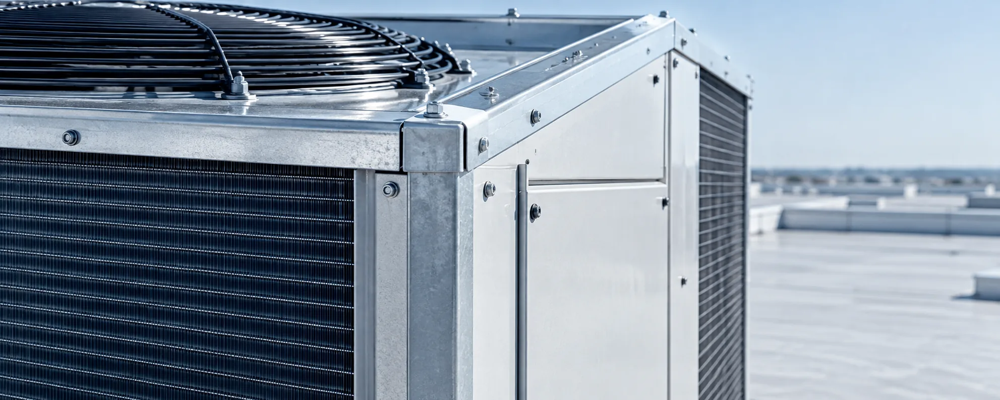 Close-up of a commercial rooftop air-conditioning unit: condenser coil, fan guard and galvanized corner panels against a clear sky